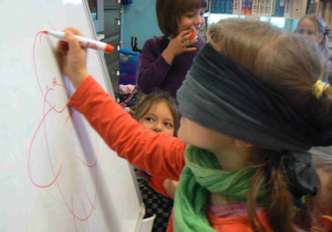 Dziecko rysuje na tablicy misia z zawiązanymi oczami